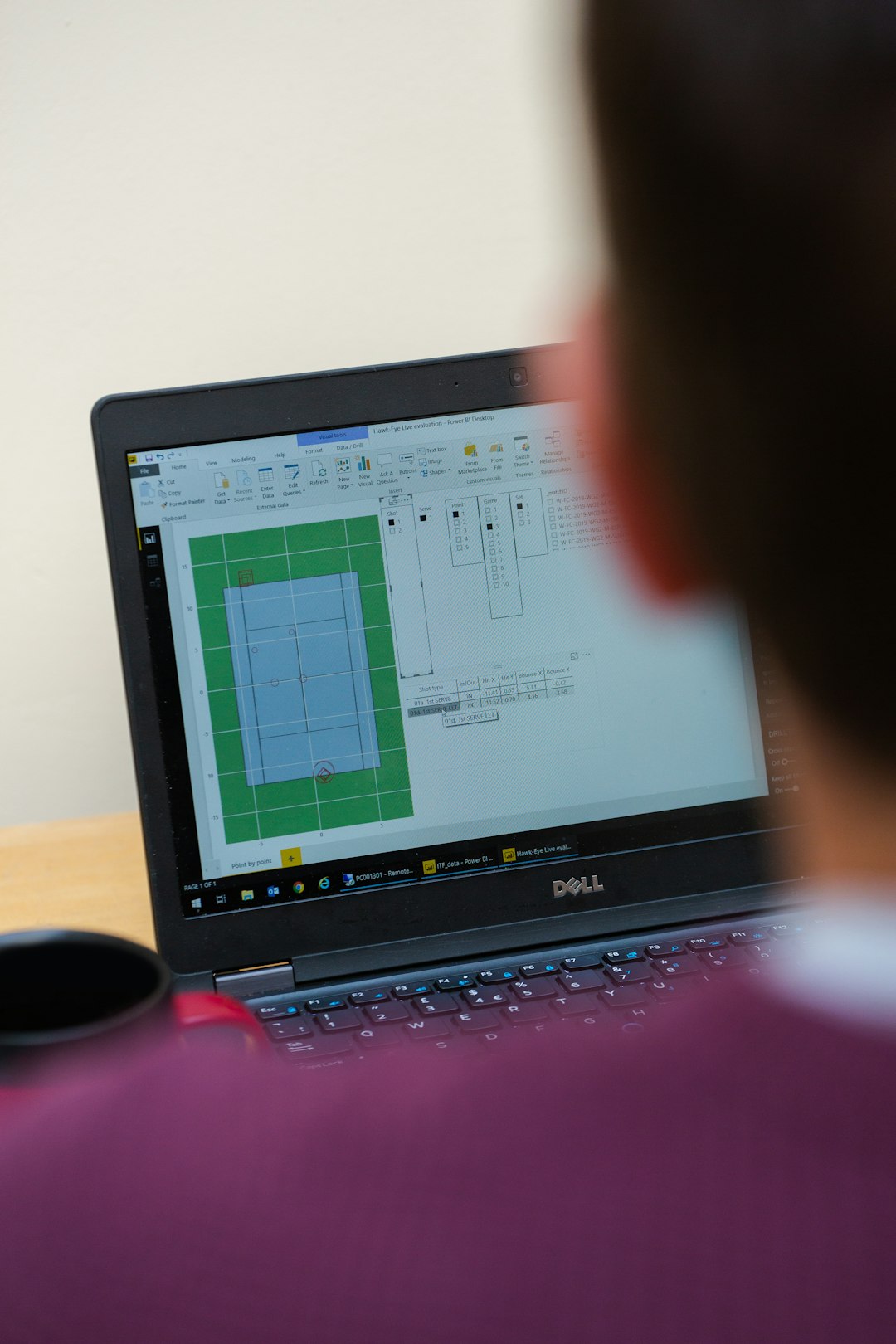 Male sports engineer analyses tennis court on computer by Uniphonic black laptop computer turned on on brown wooden table